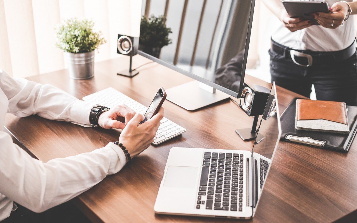Person sitzt mit Handy vor Laptop
